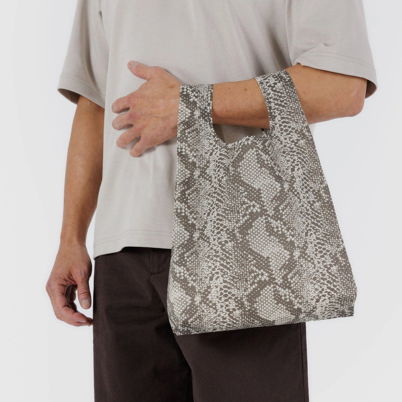 Someone carries a chic gray Baby Baggu Reusable Bag in a snakeskin pattern made from recycled nylon, elegantly draped at their side.