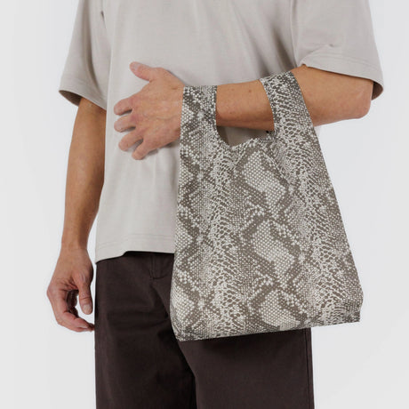 Someone carries a chic gray Baby Baggu Reusable Bag in a snakeskin pattern made from recycled nylon, elegantly draped at their side.