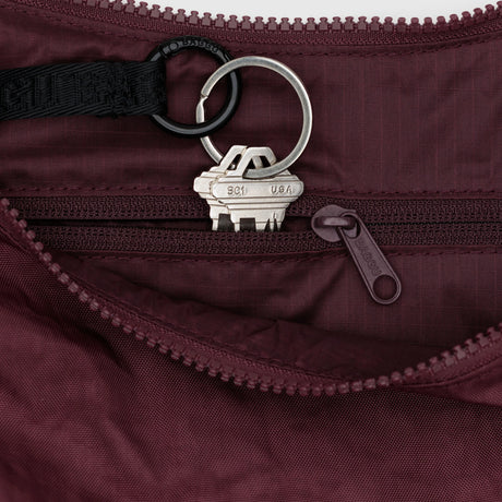 A set of keys on a keyring and black strap rests inside the small zippered pocket of the mahogany Baggu Medium Crescent Bag by Baggu.
