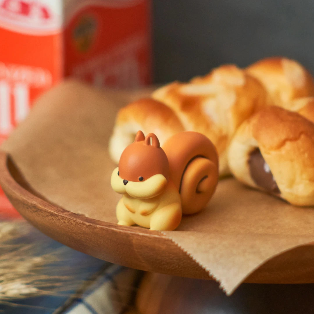 A small brown squirrel from the Dreams Inc Animal Bakery Blind Box - Vol 2 sits on a wooden tray beside chocolate pastries, creating a charming Animal Bakery scene.
