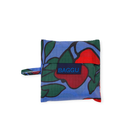 The Baggu Baby Baggu Bag - Apple Tree, a folded reusable bag with a colorful apple print and small carrying loop, is shown against a white background.