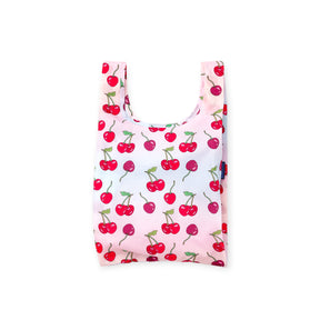 Folded reusable shopping bag with bright red and dark red cherries and green stems on a pale pink background