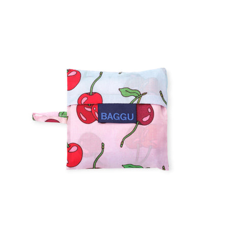 Folded reusable bag with bright red cherries and green leaves on pink and light blue fabric featuring a navy blue label