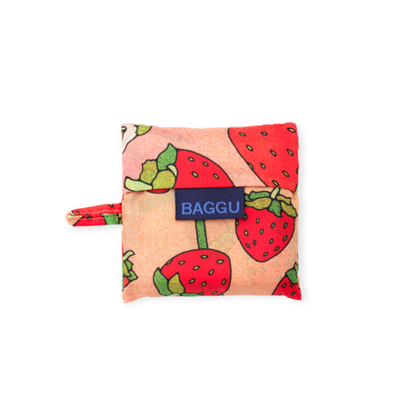 Compact folded reusable bag with red strawberries and green leaves on a soft pink background and navy blue label
