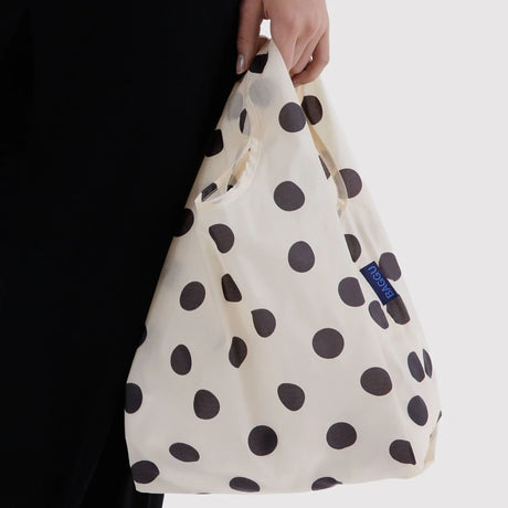 Cream baby tote bag with black polka dots, held by hand with blue logo patch