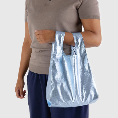 A person holding the Baggu Baby Baggu Bag in metallic light blue against a neutral background.