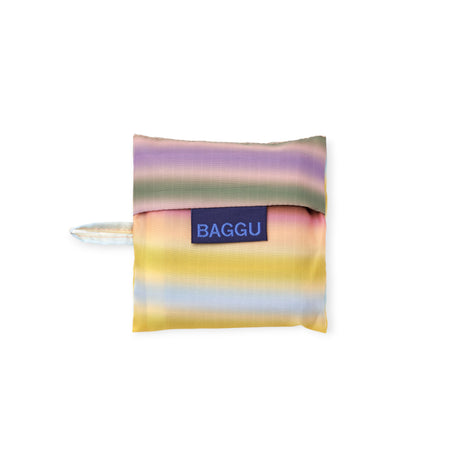 Compact folded reusable bag with soft horizontal stripes in pastel yellow, lavender, pink, and green featuring navy blue label