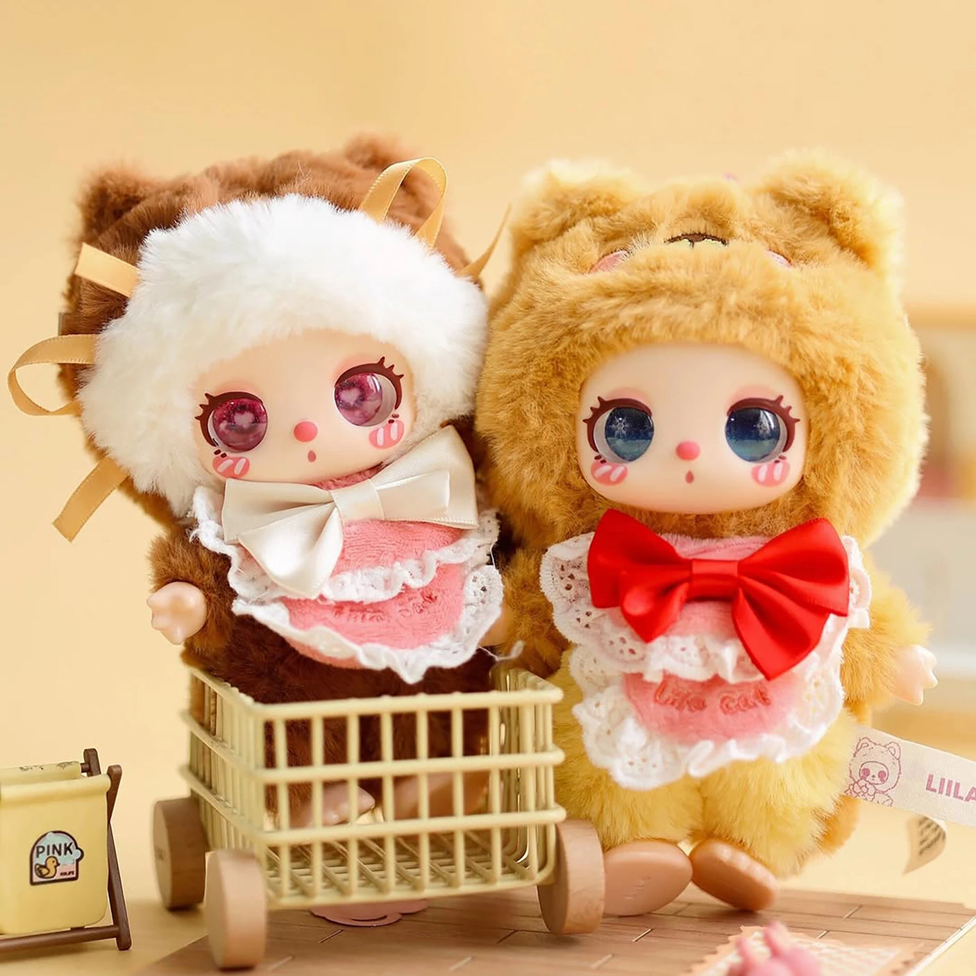 Baby Three - Liila's Chef Kitten Blind Box dolls in fluffy animal onesies with lace bibs and large bows, one in cart and one standing.