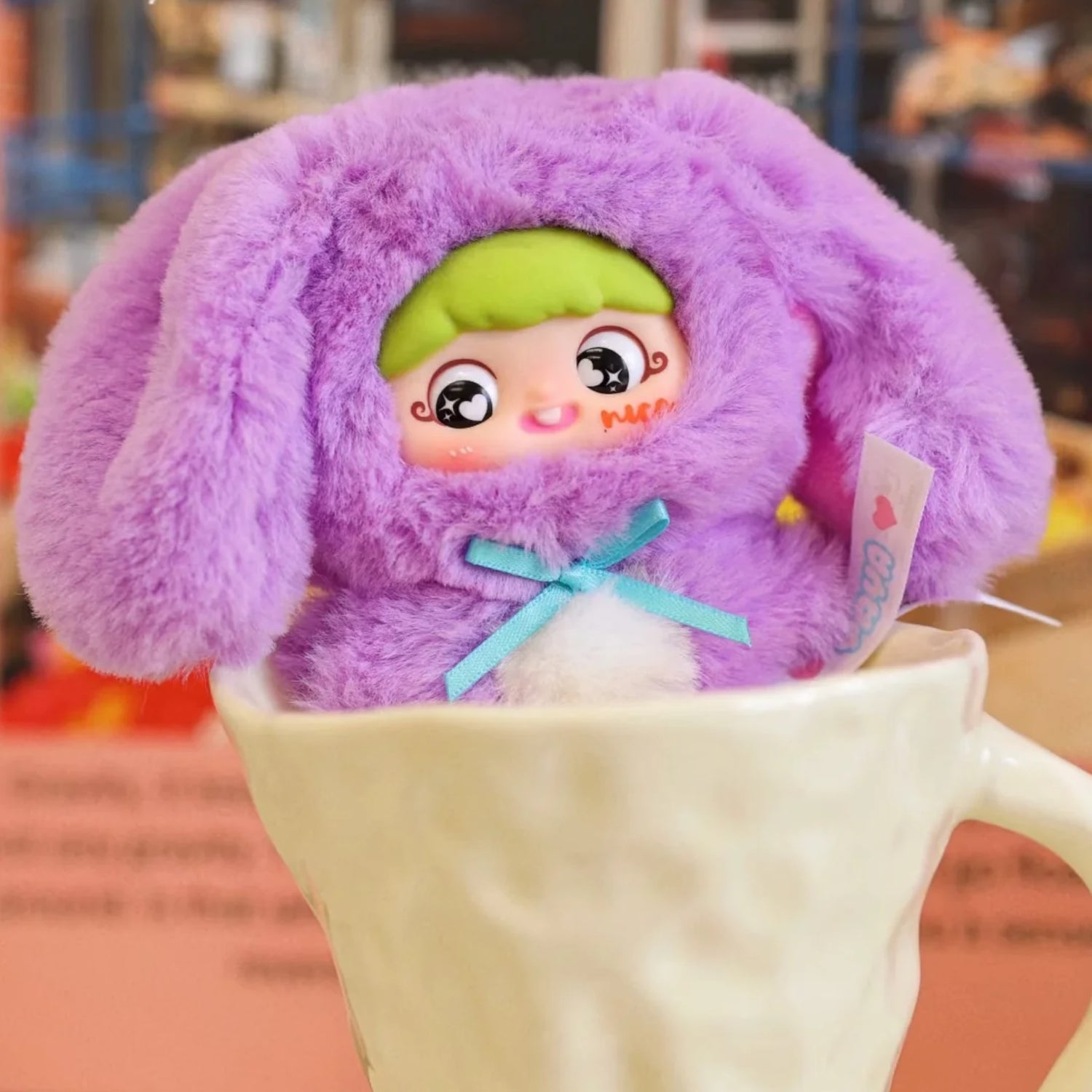 Baby Three x YAYA - Birthday Plush Pendant Blind Box doll in a purple bunny onesie with green hair and blue ribbon inside a white cup