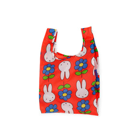 The Baby Baggu x Miffy Flower by Baggu is a red reusable shopping bag featuring white cartoon bunnies and blue flowers.