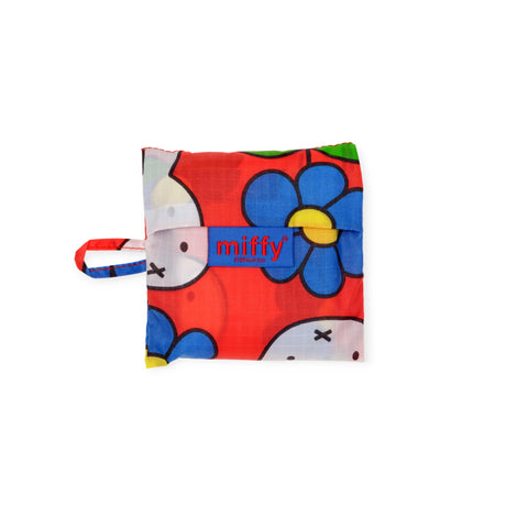 A folded Baggu Baby Baggu x Miffy Flower reusable bag with a red background, Miffy faces and blue flowers, a small handle on the left, and "miffy" printed on the front—a cute collab between Baggu and Miffy.
