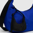 The Baggu Crescent Bag Charm in Cornflower is a vibrant blue shoulder bag made from recycled nylon, with a textured black strap and an attached small black pouch, set against a plain light background.