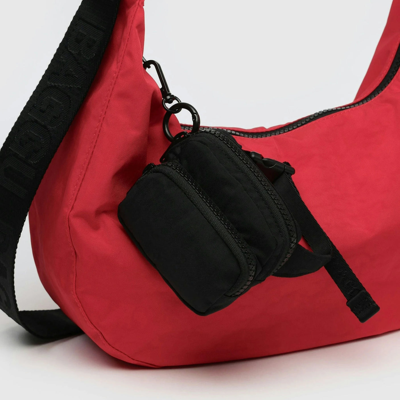 The Baggu Fanny Pack Charm by Baggu is a stylish red bag with a black strap, made from recycled heavyweight nylon. It includes a small, black zippered pouch, making it the perfect accessory for minimalistic style and functionality.