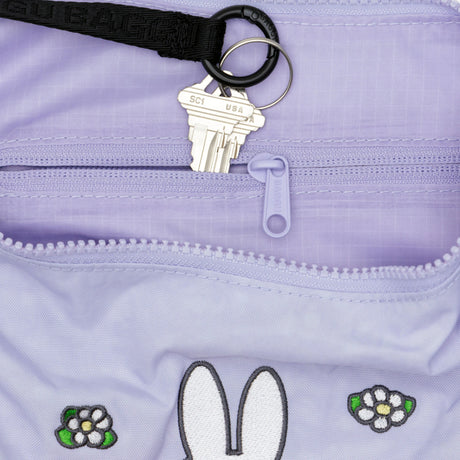 A pair of silver keys on a black keychain sits atop the Baggu Miffy x Baggu Medium Nylon Crescent, a lavender crossbody bag featuring whimsical flower and bunny ear designs.