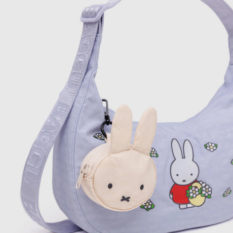 The Baggu Miffy x Baggu Medium Nylon Crescent is a lavender crossbody with a Miffy cartoon print and a small beige Miffy-shaped coin pouch on the strap, perfect for fans of the adorable Miffy x Baggu collection.