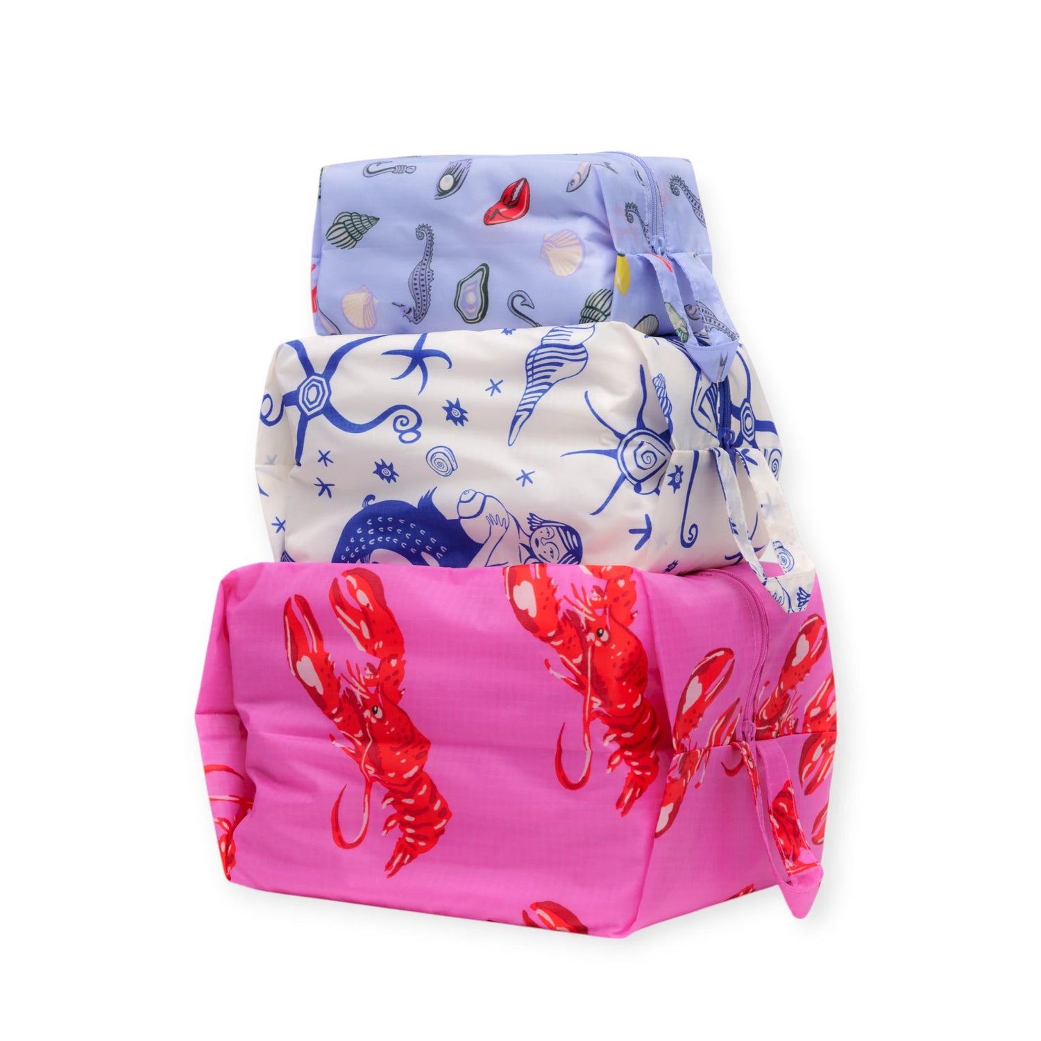 Three rectangular gifts wrapped in colorful fabric—blue with seashells, white with blue sea creatures, and pink with red lobsters—ideal for storing surprises or organizing essentials like the Baggu Storage & Travel Set - Sea Creatures.