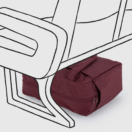 A Baggu Small Cloud Carry-on in mahogany, featuring a zipper and handles, sits under a digitally illustrated airplane seat.