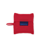 The Candy Apple Baby Baggu Reusable Bag by Baggu is a stylish and sustainable red fabric pouch, made from 100% recycled nylon. It features a handle, folds neatly, and is adorned with a blue label that reads "BAGGU.