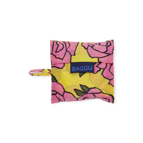 A folded Baggu Baby Baggu Reusable Bag in the Rose design features a delightful pink rose pattern set against a cheerful yellow backdrop, made from recycled nylon.