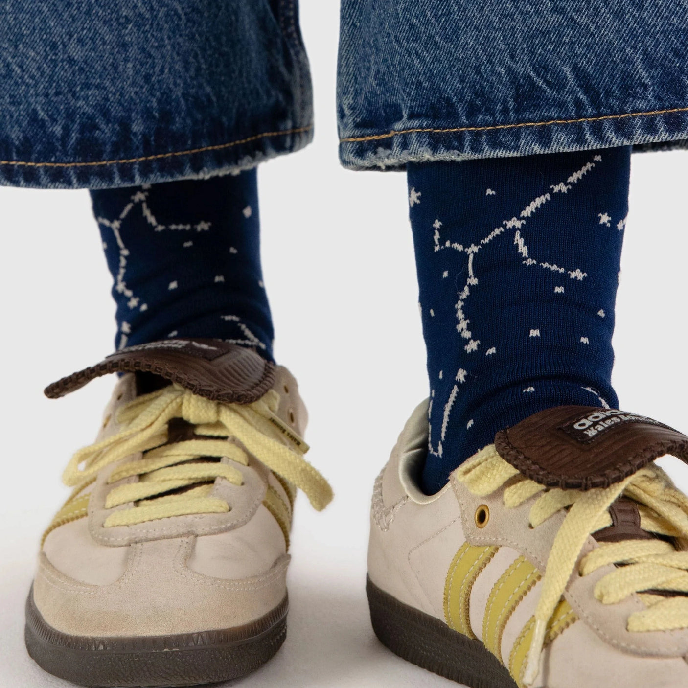 A person wearing jeans and fashionable Baggu Crew Sock - Constellation Midnight, complemented by beige sneakers with striking yellow stripes.