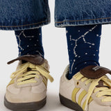 A person wearing jeans and fashionable Baggu Crew Sock - Constellation Midnight, complemented by beige sneakers with striking yellow stripes.