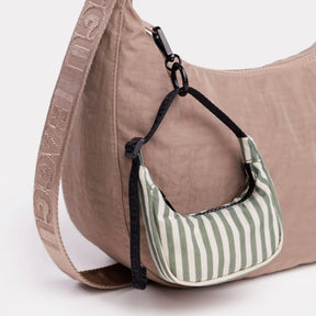 Striped crescent bag charm with black loop, hanging on a beige bag