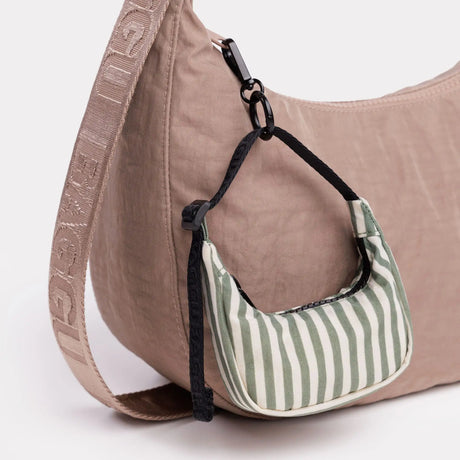 Striped crescent bag charm with black loop, hanging on a beige bag
