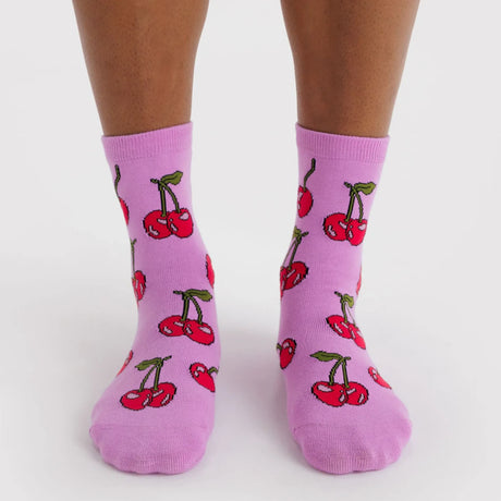 Pair of pink crew socks with scattered red cherries and green leaves