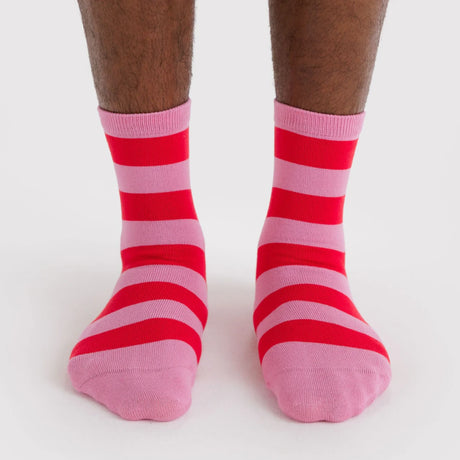 Pair of crew socks featuring bold horizontal stripes in alternating pink and red worn on feet against white background