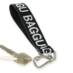 A set of keys hangs on a metal ring attached to the Baggu Keychain - Logo Strap, featuring a black and white design crafted from eco-friendly recycled nylon webbing.