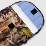 A Baggu Puffy Laptop Sleeve 16" in the Photo Forest camouflage pattern is partially open, revealing a light blue interior and a white laptop inside. Made from recycled nylon, it seamlessly blends style with sustainability.