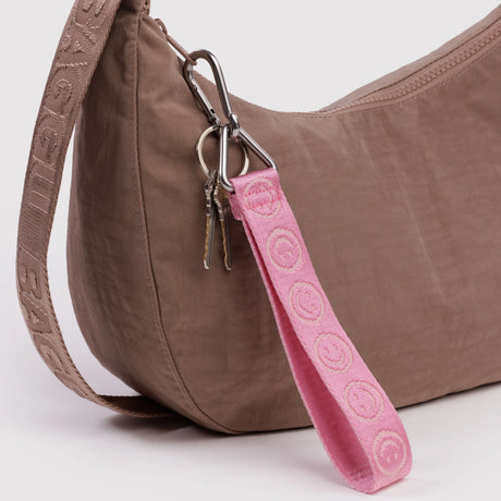 Brown fabric shoulder bag with beige strap and attached pink wrist keychain with smiley face embroidery