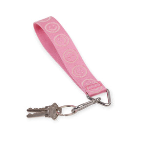 Pink fabric keychain wrist strap with embroidered smiley faces and attached metal keys on white background