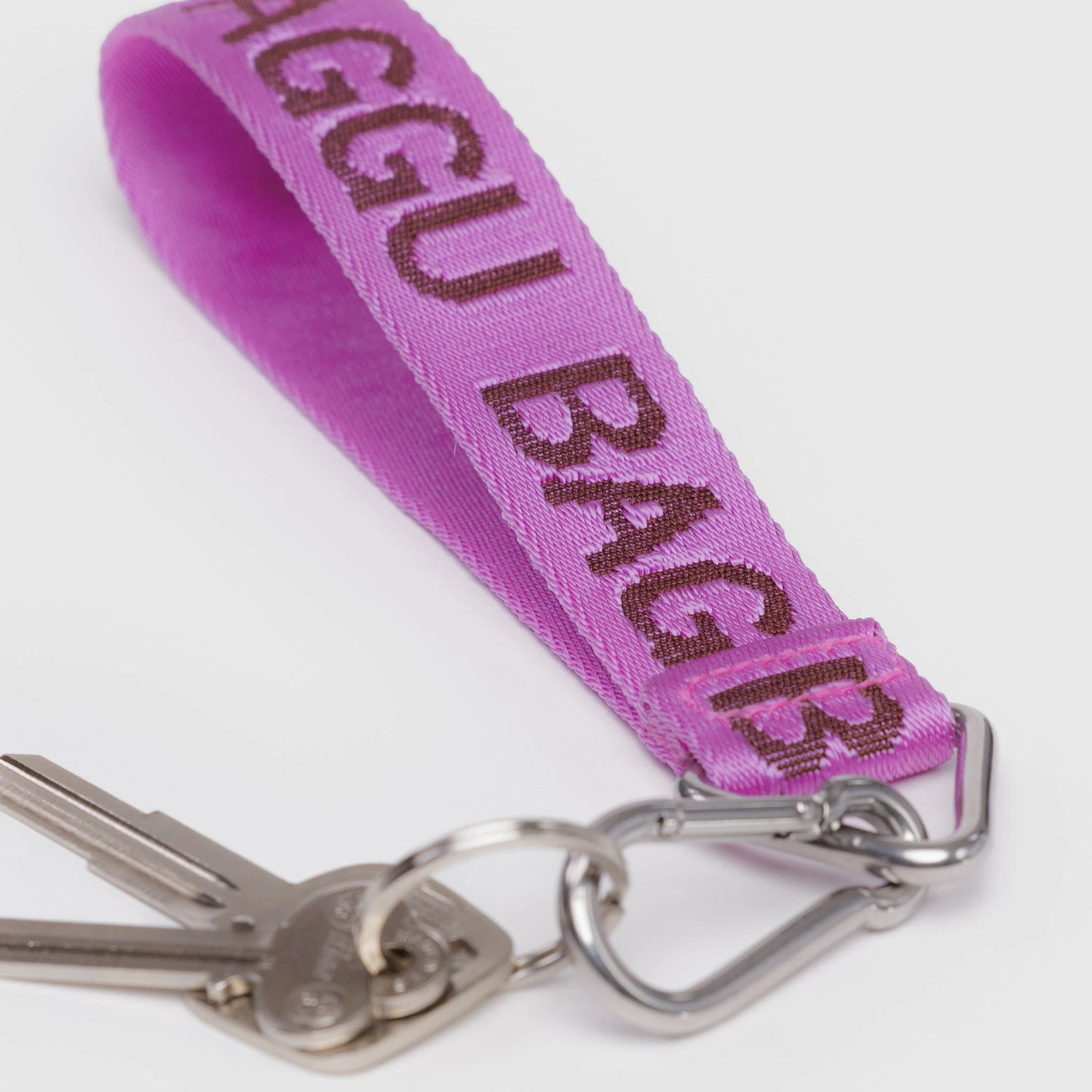 The Baggu Logo Keychain - Pink by Baggu features silver keys on a metal clip and a pink recycled nylon strap with "BAGGU BAGGU" in bold dark letters.