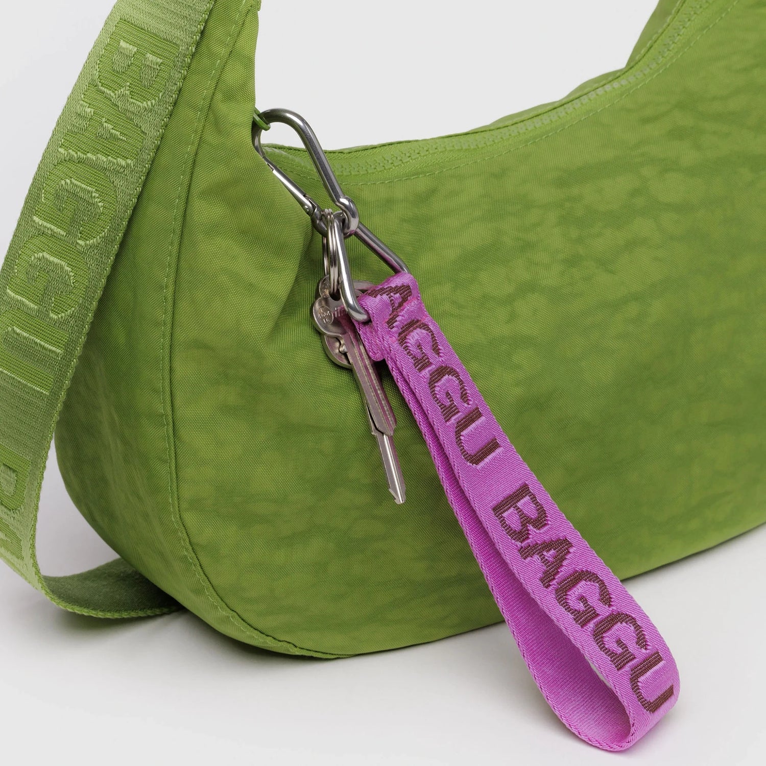A green BAGGU bag with a matching strap, a Baggu Logo Keychain - Pink, and a set of keys connected by a silver carabiner showcase the playful style of the pink Baggu Logo Keychain.