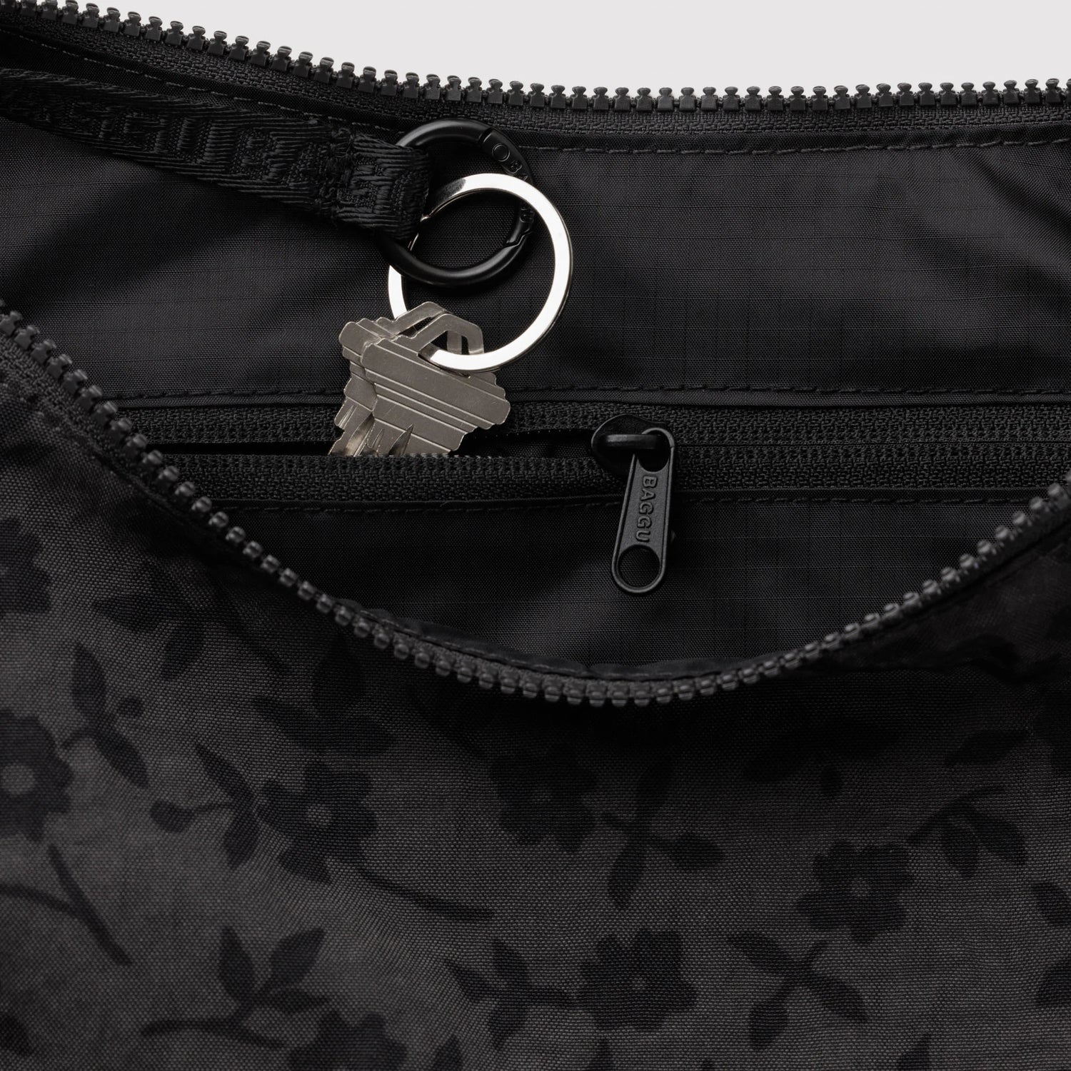 Dark nylon crescent bag interior detail: zip, ring pull, and lobster clasp hardware