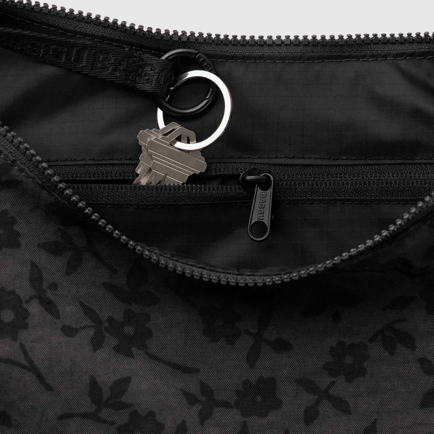 Dark nylon crescent bag interior detail: zip, ring pull, and lobster clasp hardware