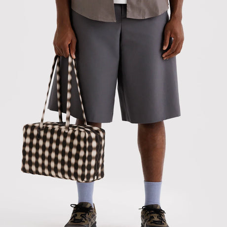 Rectangular fabric handbag with black and beige geometric pattern and long thin straps held by person in gray shorts