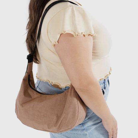 A person in a beige top and blue jeans carries a chic Baggu Medium Nylon Crescent Bag - Cocoa, made from recycled ripstop nylon.