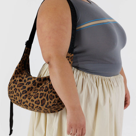 A person in a gray sleeveless top and beige skirt is holding a Baggu Medium Nylon Crescent Bag - Leopard.