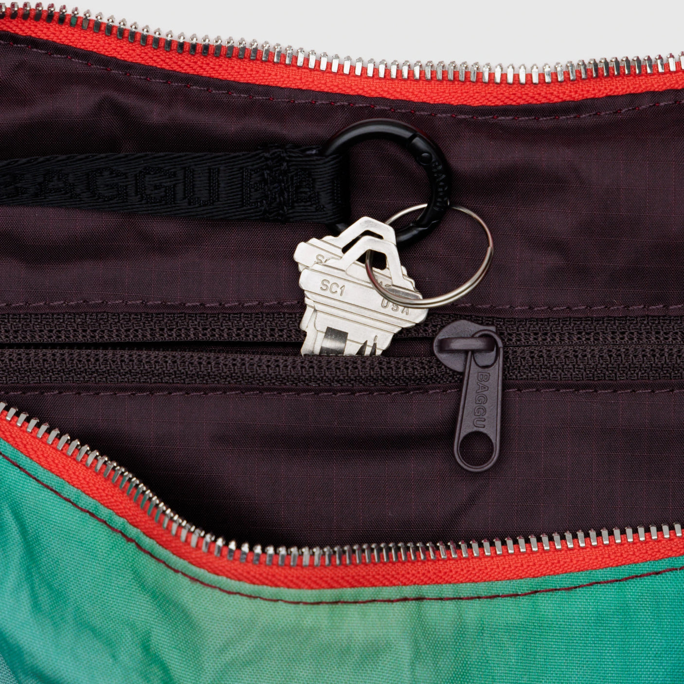 Inside the dark zipper pocket of a Baggu x Julia Heuer - Medium Nylon Crescent Rain bag, a silver key on a black keyring highlights limited edition sustainable style.