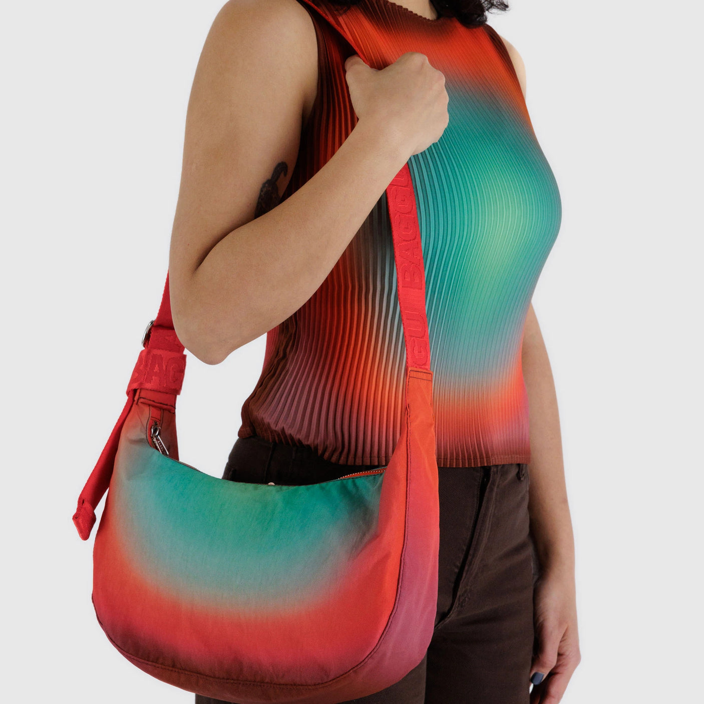 A person stylishly carries a Baggu x Julia Heuer - Medium Nylon Crescent Rain over their shoulder, showcasing a sleeveless gradient top with dark pants. Crafted from recycled nylon, this eco-chic bag enhances the vibrant ensemble with style.