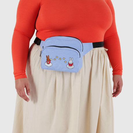 A person wearing a red-orange long sleeve top, cream skirt, and a blue Baggu Miffy x Baggu Fanny Pack made from recycled nylon, featuring cartoon bunnies and stars.
