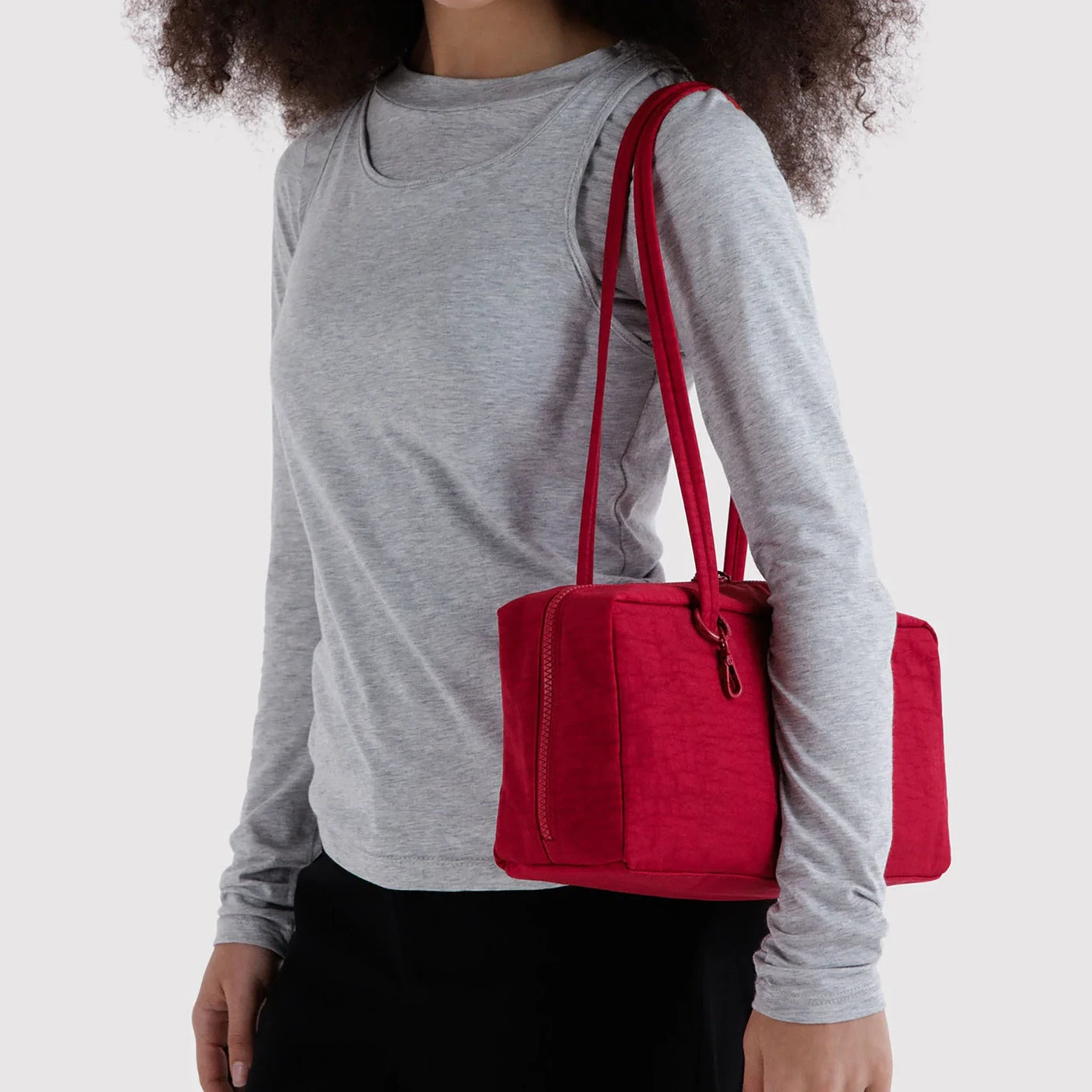Nylon bowler bag in cherry red, carried by handles on a person in a gray top