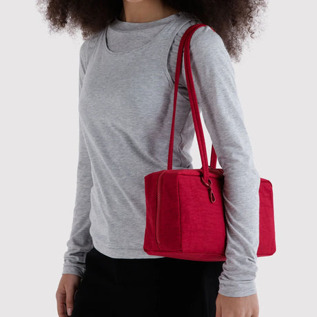Nylon bowler bag in cherry red, carried by handles on a person in a gray top