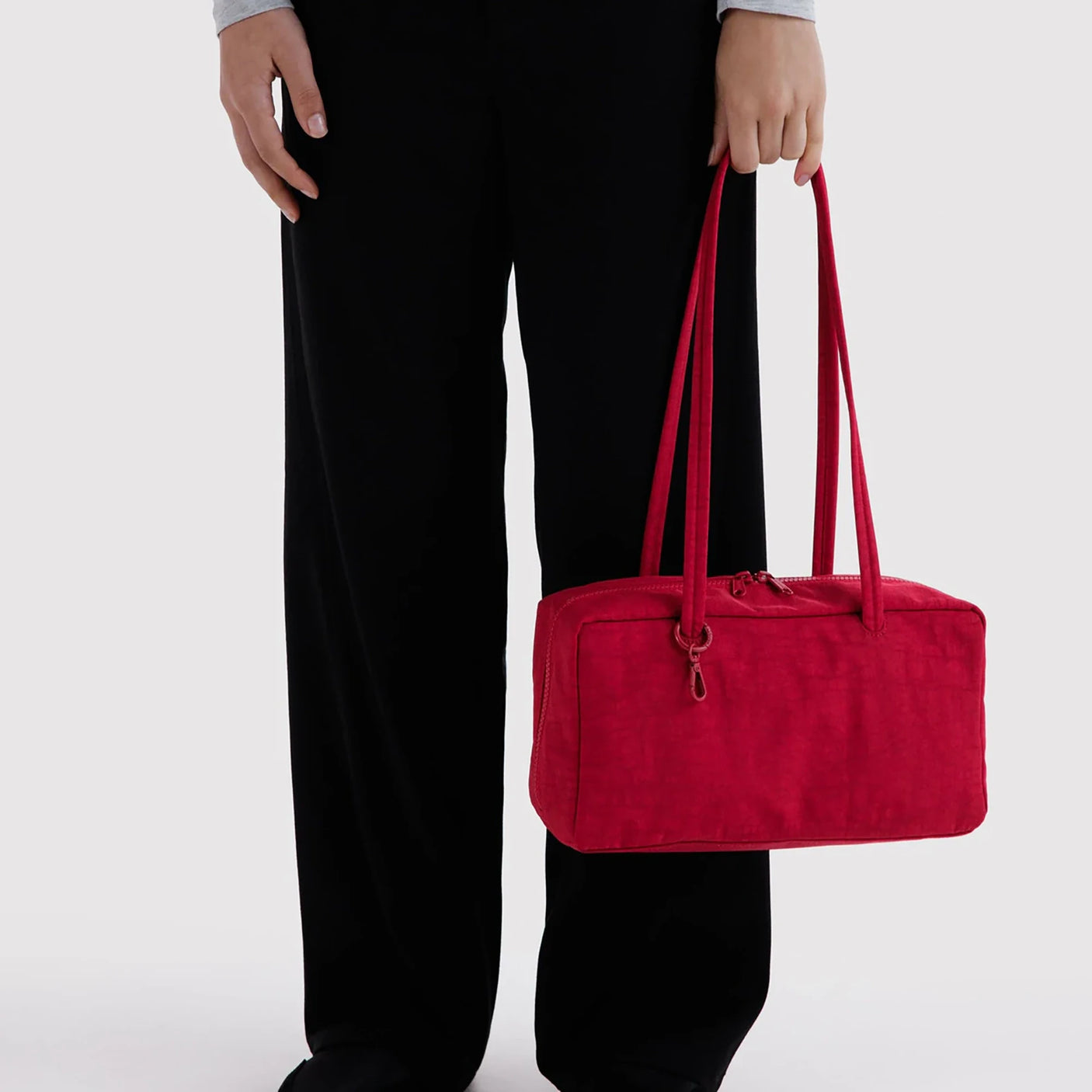 Nylon bowler bag in cherry red, carried by rolled handles beside black pants