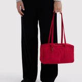 Nylon bowler bag in cherry red, carried by rolled handles beside black pants