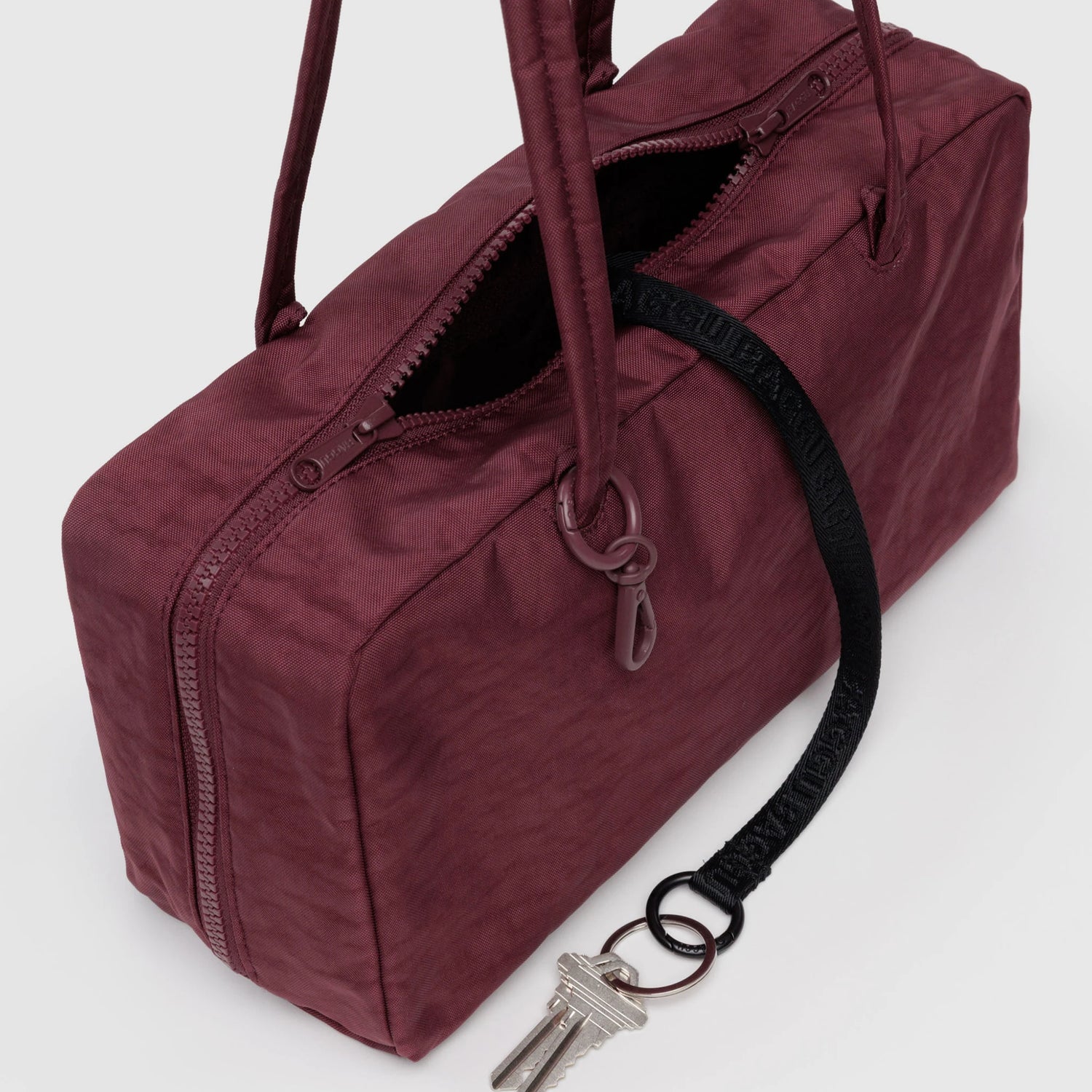 A Baggu Nylon Bowler Bag - Mahogany by Baggu, rectangular with a zipper, dual handles, and a black key leash attached to a pair of keys.