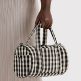 Nylon duffle bag in black-and-cream gingham, top handle held in hand