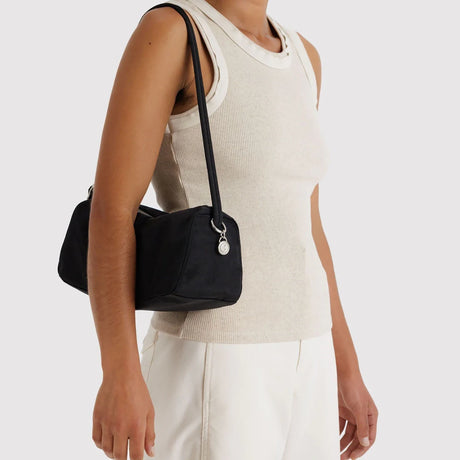Black small rectangular shoulder bag with long strap and silver round zipper pull worn over shoulder